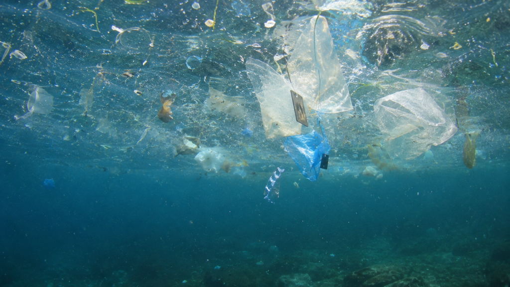 Underwater scene filled with floating plastic bags and trash drifting in the blue ocean water.