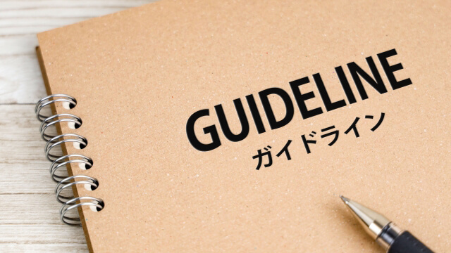 Spiral-bound notebook on a light wood surface with the word GUIDELINE and ガイドライン, plus a pen nearby.