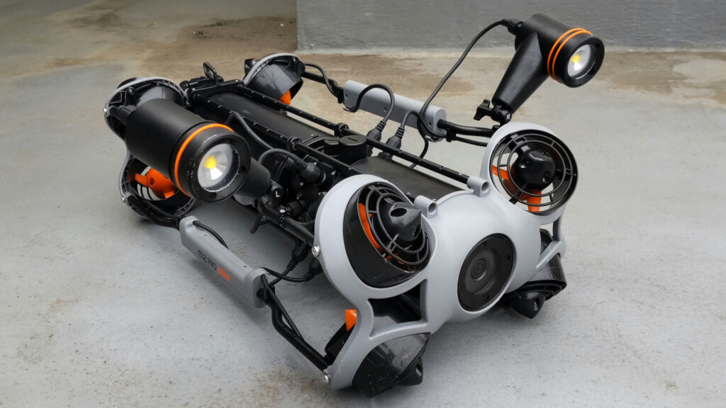 Industrial-looking robot chassis with four circular fans and orange accents on a rough concrete floor.