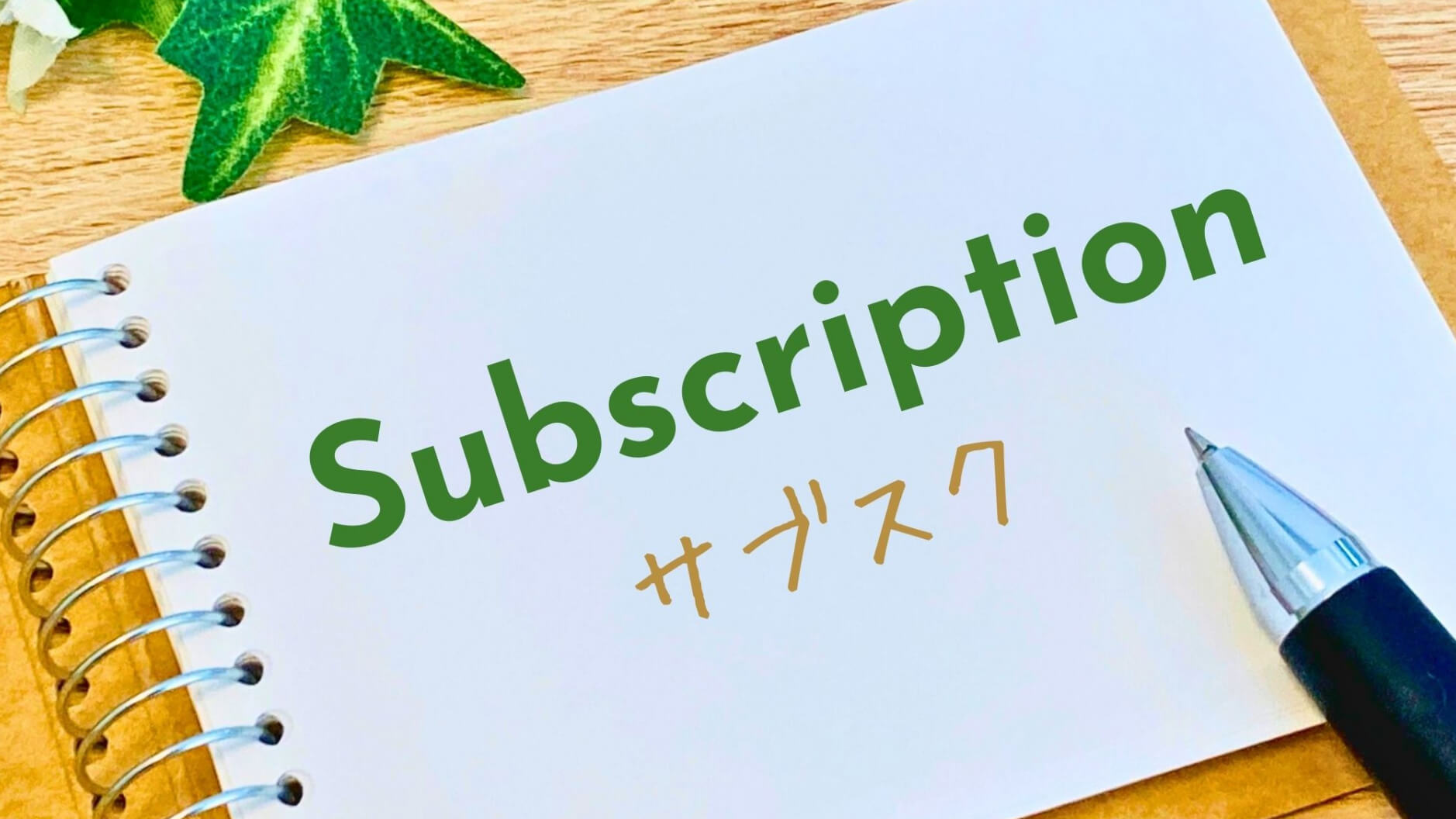 Notebook page shows the word 'Subscription' in green letters with a blue pen nearby on a wooden desk, conveying a subscription concept.