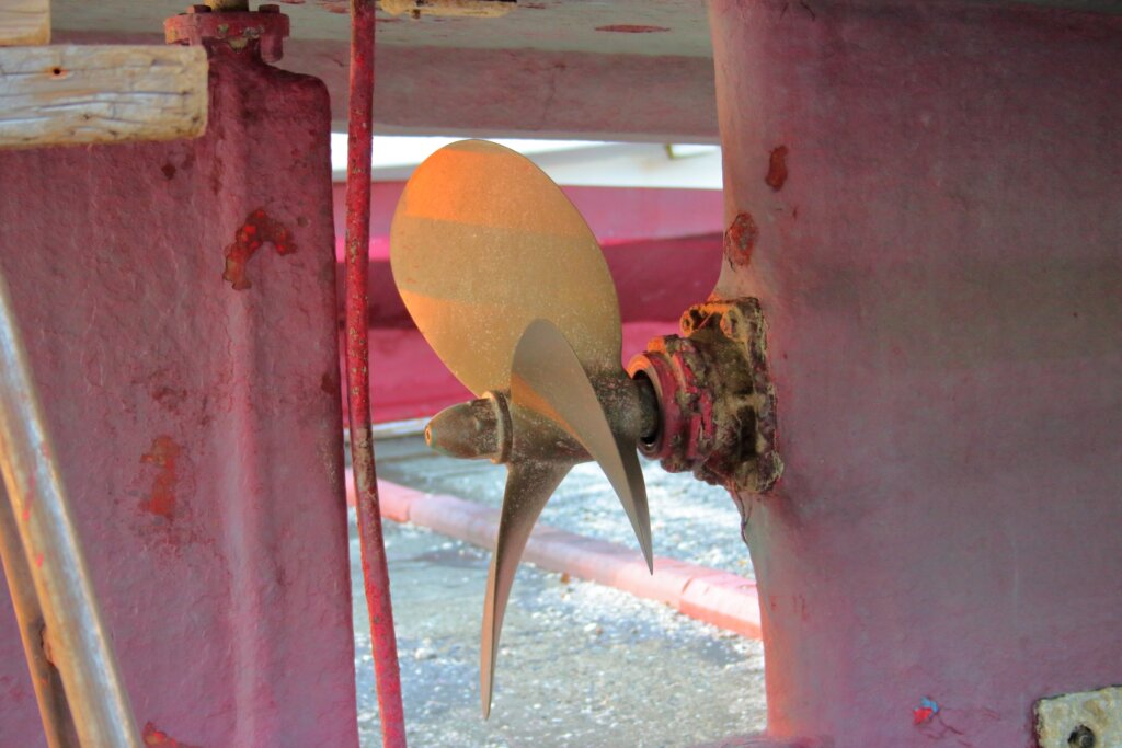 船のスクリュー - 株式会社SeaChallenge - 株式会社SeaChallenge Three-blade boat propeller mounted inside a rusted red hull, showing wear and peeling paint.